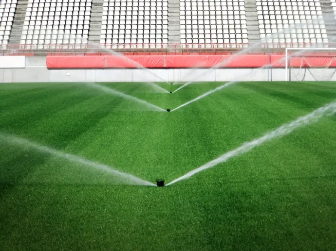 Mehrere Versenkregner bewässern Naturrasenfläche auf einem Sportplatz im Stadion