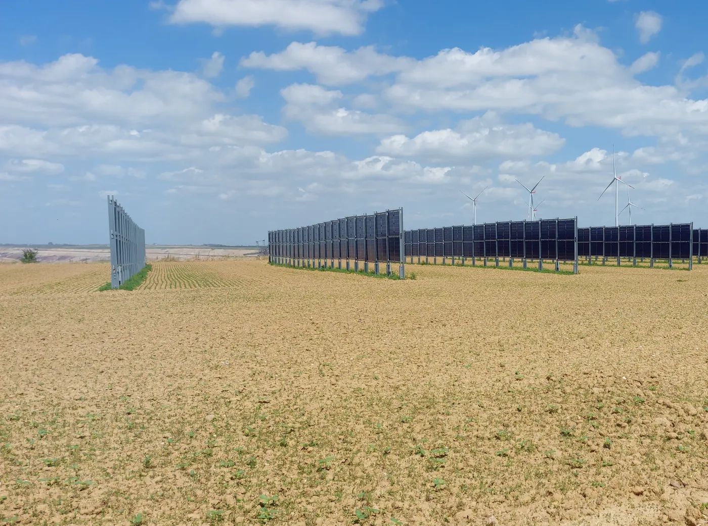 Senkrechte Solarmodule am Rand des Tagebaus, Windräder im Hintergrund